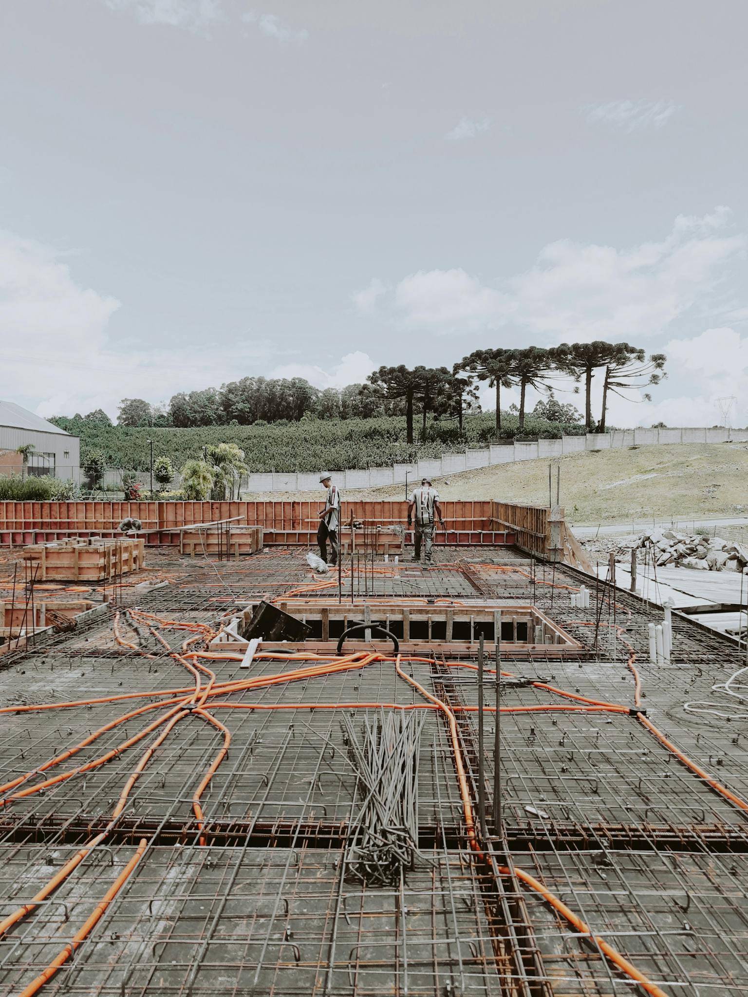 Outdoor construction site with visible steel framework and workers, set against a clear sky.